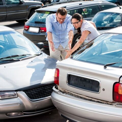 Ein Parkplatzunfall mit zwei Autos, Front an Heck. Daneben gestikulieren eine Frau und ein Mann.