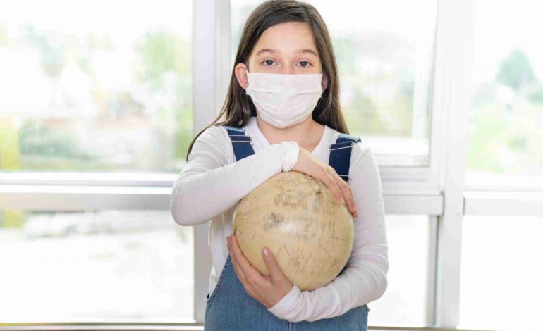 Mädchen mit Mundschutz hält einen Globus in den Händen