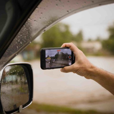 Ein Mann hält sein Smartphone zum Autofenster hinaus, um etwas zu filmen.