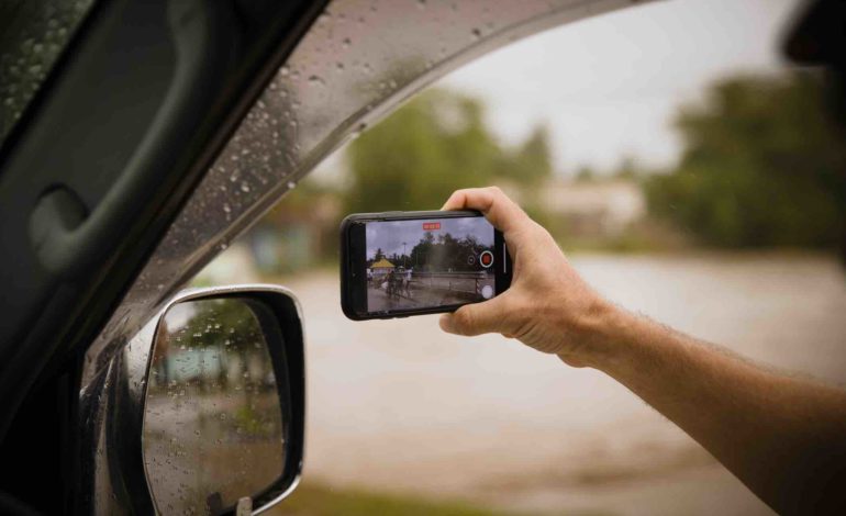 Ein Mann hält sein Smartphone zum Autofenster hinaus, um etwas zu filmen.