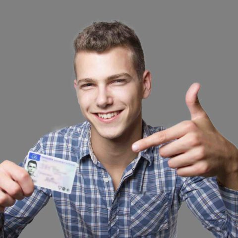 Lächelnder junger Mann hält seinen Führerschein hoch und zeigt darauf.