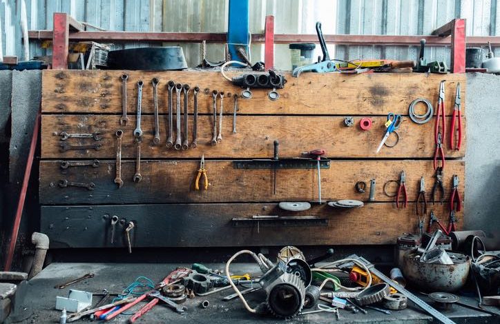 Verschiedene Werkzeuge liegen durcheinander in der Werkstatt der Garage. Alte Schraubenschlüssel hängen an der Holzwand darüber.