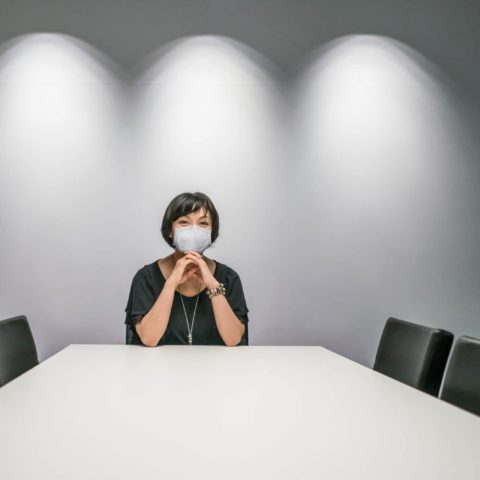 Vereins- und Gesellschaftsrecht: Eine Frau mit Mund-Nasen-Maske sitzt alleine an einem großen Tisch in einem Sitzungssaal. Die anderen vier Stühle sind leer.