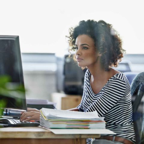 Junge Frau sitzt am Schreibtisch vor Ihrem Computer.