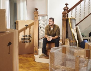 Ein Mann sitzt in seiner Wohnung auf einer Treppe. Um ihn herum stehen verpackte Möbel und Kartons. Er wirkt bedrückt. Kündigung durch Vermieter.