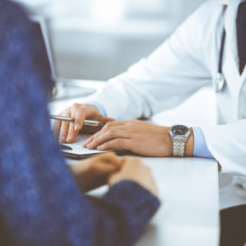 Hände und Schultern zweier Menschen. Patientin sitzt mit Ärztin am Tisch und bespricht ihre Wiedereingliederung.