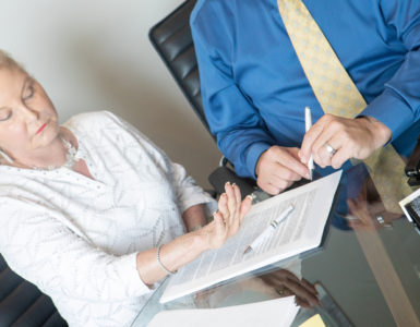 Eine Frau sitzt mit einem Mann am Tisch vor einem Rechtsdokument und hebt die Hand zum Widerspruch.
