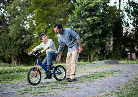 Sorgerecht und Umgangsrecht: Ein Junge und sein Vater in einem Park. Der Junge sitzt auf einem Fahrrad, der Vater schiebt es an.