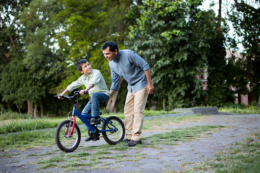 Sorgerecht und Umgangsrecht: Ein Junge und sein Vater in einem Park. Der Junge sitzt auf einem Fahrrad, der Vater schiebt es an.