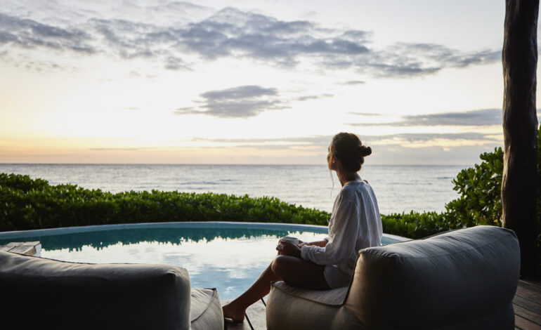 Eine Frau sitzt auf einem Sessel am Pool und genießt ihren Urlaubsanspruch, im Hintergrund das Meer.