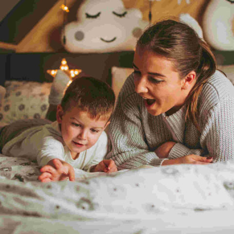 Mutter und Sohn liegen auf dem Bauch im Bett und bestaunen etwas auf dem Bett.