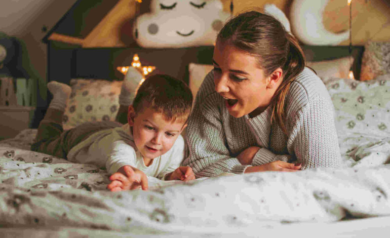 Mutter und Sohn liegen auf dem Bauch im Bett und bestaunen etwas auf dem Bett.