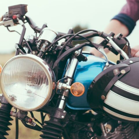 Frontansicht der Motorradbeleuchtung eines geparkten Motorrads, die Hände des Fahrers und der Helm sind auch zu sehen.