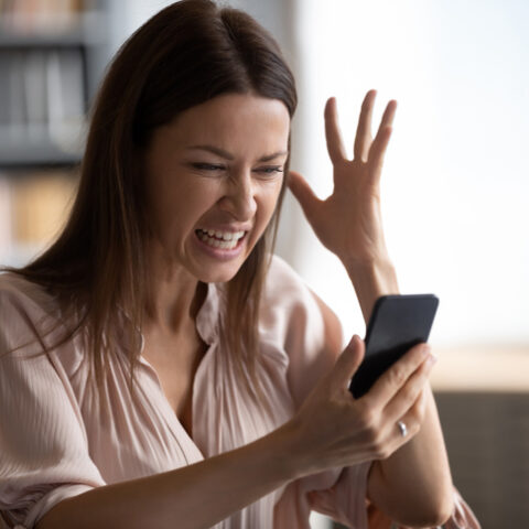 Frau mit Smartphone ärgert sich mit hochgehaltener Hand über unerwünschte Werbung.
