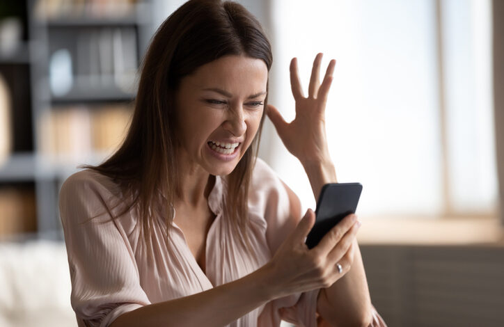 Frau mit Smartphone ärgert sich mit hochgehaltener Hand über unerwünschte Werbung.