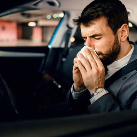 Mann im Anzug fährt krank Auto und putzt seine Nase.