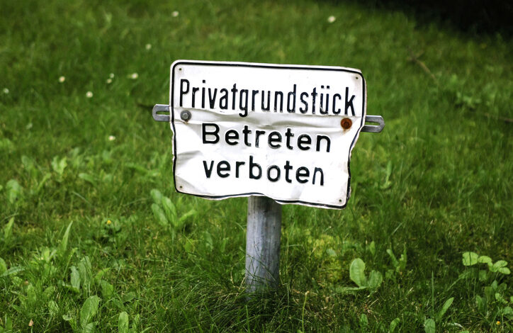 Ein kleines verbeultes Schild auf einer Wiese, das Hausfriedensbruch vorbeugen soll. Darauf steht Privatgrundstück, Betreten verboten.
