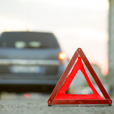 Das Verhalten nach einem Verkehrsunfall beinhaltet das Aufstellen eines Warndreiecks. Im Hintergrund sieht man ein Auto von hinten.