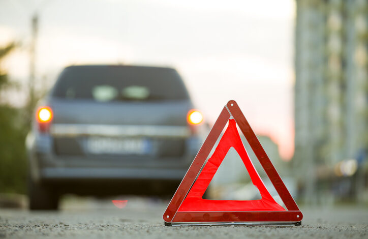 Das Verhalten nach einem Verkehrsunfall beinhaltet das Aufstellen eines Warndreiecks. Im Hintergrund sieht man ein Auto von hinten.