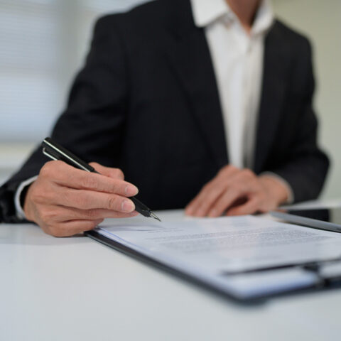 Eine Person im Anzug sitzt an einem Tisch und unterschreibt eine Abfindung.