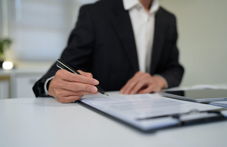 Eine Person im Anzug sitzt an einem Tisch und unterschreibt eine Abfindung.
