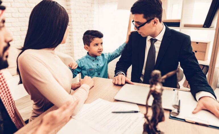 Junge Eltern, Mutter und Vater, diskutieren an einem Tisch über das Sorgerecht mit einem jungen Anwalt in Anzug und Krawatte. Daneben steht der Sohn, ein kleiner Junge. Auf dem Tisch sind Stifte, Papier und eine Statue von Justizia.
