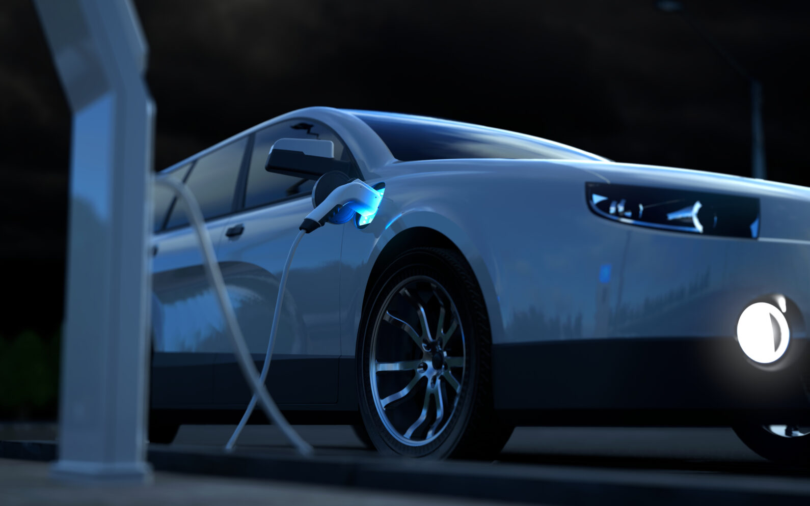 Ein weißes E-Auto bei Nacht, das an einer Ladesäule aufgeladen wird.