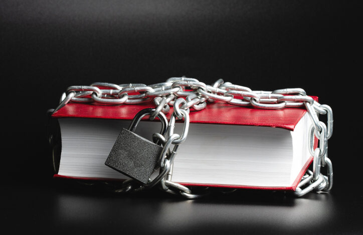 Preisgebunden: Ein rotes Buch auf dem Tisch, in Ketten gelegt, mit einem Vorhängeschloss.