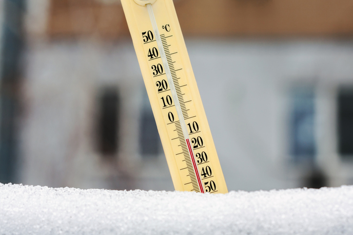 Ein analoges Thermometer steckt im Schnee und zeigt minus 12 Grad an.