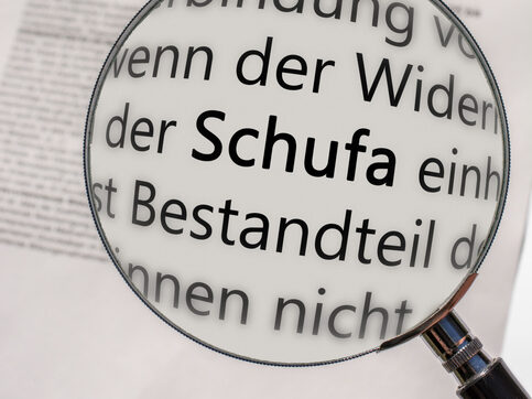 Eine Lupe, die unter anderem das Wort Schufa vergrößert.