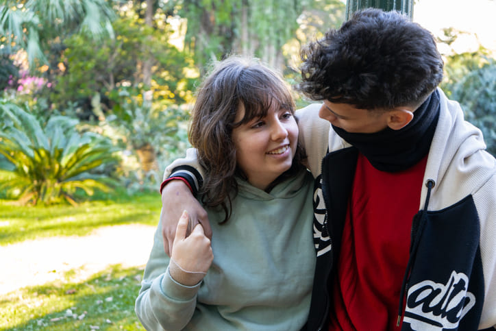 Darf man mit 14 eine Beziehung haben? Ein junges Paar in einem Park, das sich verliebt ansieht.
