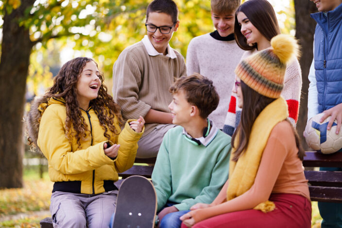 Was darf man mit 14? Eine Gruppe Jugendlicher mit bunter Kleidung unterhält sich an einer Bank im Park.