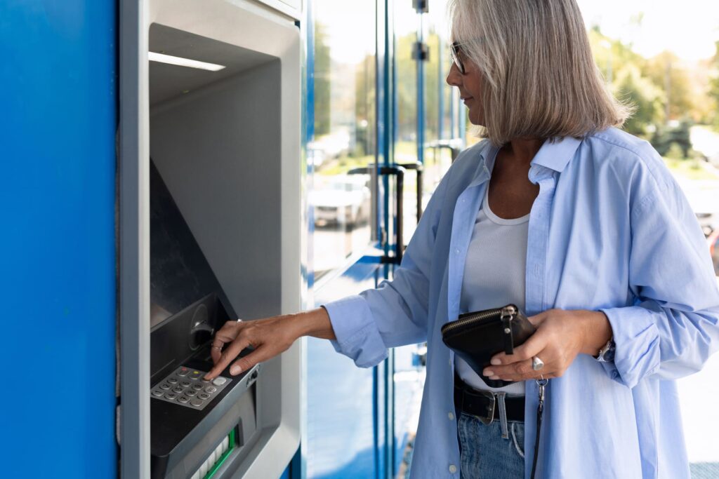 Neuerungen März 2026 bei der Rente: Rentnerin steht mit Geldbeutel in der Hand am Bankautomat.