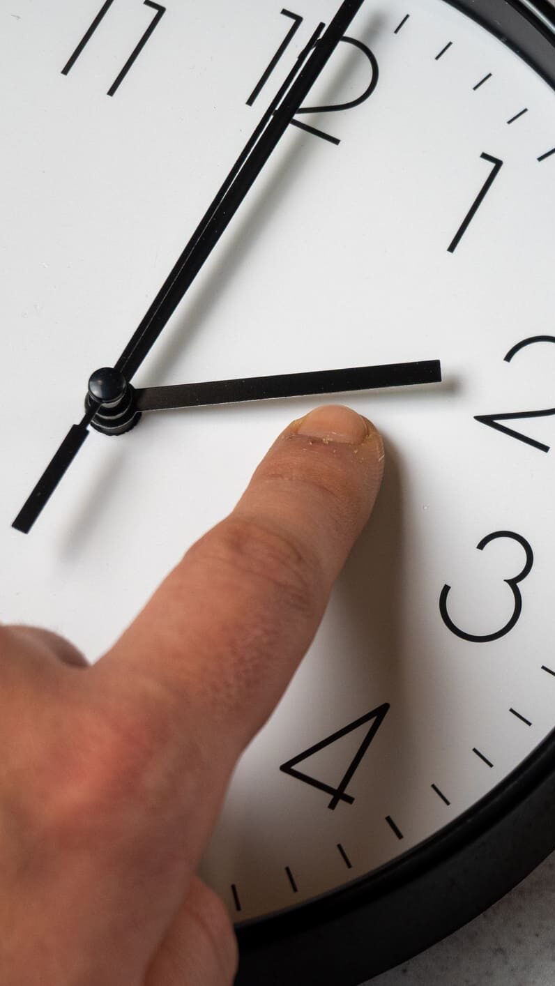Sommerzeit März 2026: Eine analoge Uhr und ein Finger, der den Stundenzeiger verschiebt.