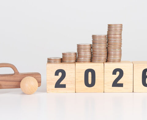 Bauklötze mit der Zahl 2026, daneben ein Auto aus Holz und darüber Stapel mit Münzen, um die E-Auto-Förderung zu symbolisieren.