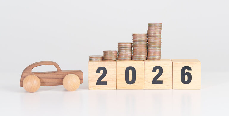 Bauklötze mit der Zahl 2026, daneben ein Auto aus Holz und darüber Stapel mit Münzen, um die E-Auto-Förderung zu symbolisieren.