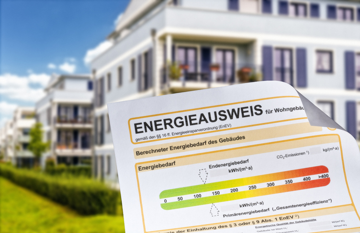 Ein Papier mit einem Energieausweis nach den Neuerungen Mai 2026, dahinter mehrere Häuser.