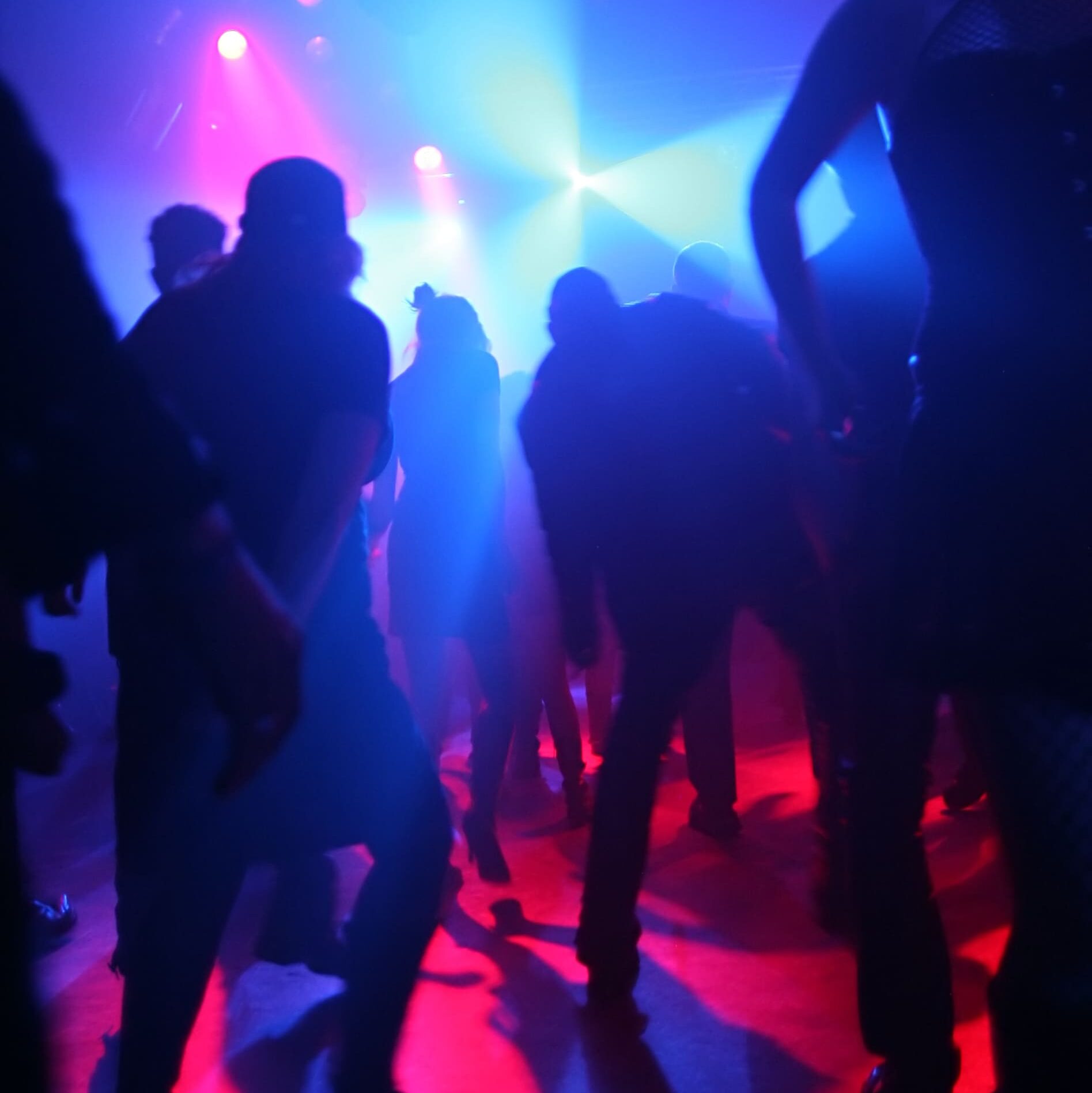 Was darf man mit 16? Silhouetten mehrerer Menschen in einer dunklen Disko, darüber Scheinwerfer mit rotem und blauem Licht.
