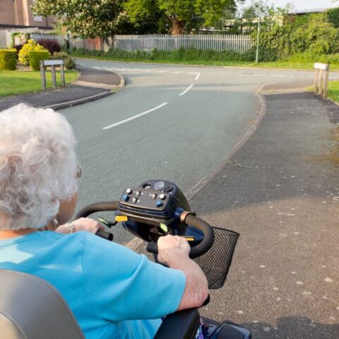 Eine Seniorin auf einem elektrischen Rollstuhl am Straßenrand hält die Promillegrenze für motorisierte Krankenfahrstühle ein.