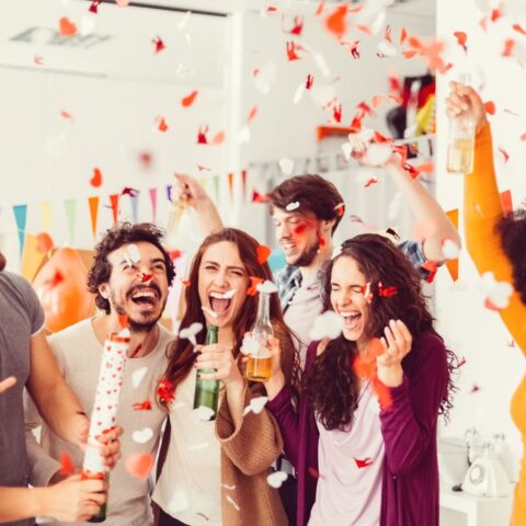 Eine Gruppe junger Menschen nutzt, was man mit 18 darf, jeder hält ein alkoholisches Getränk in der Hand und jubelt. Durch die Luft fliegt Konfetti.