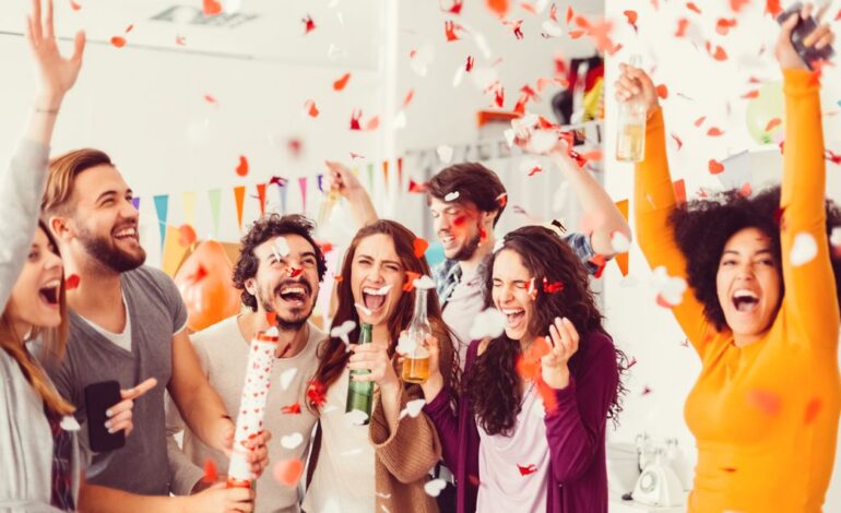 Eine Gruppe junger Menschen nutzt, was man mit 18 darf, jeder hält ein alkoholisches Getränk in der Hand und jubelt. Durch die Luft fliegt Konfetti.