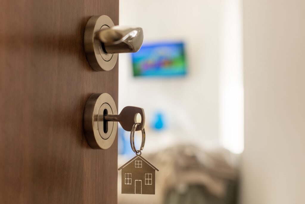 Eine geöffnete Wohnungstür, darin steckt ein Schlüssel mit einem Haus-Schlüsselanhänger. Dahinter Blick in die Wohnung und einen Fernseher an der Wand.