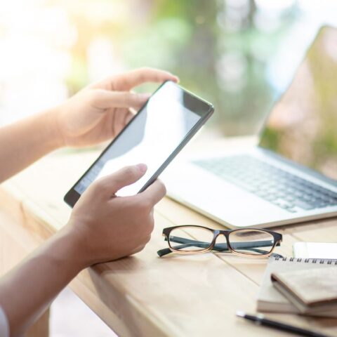Hände einer Person mit Smartphone, die eine Kündigung per WhatsApp verfasst. Vor ihr auf dem Schreibtisch ein Laptop, eine Brille, ein Geldbeutel.