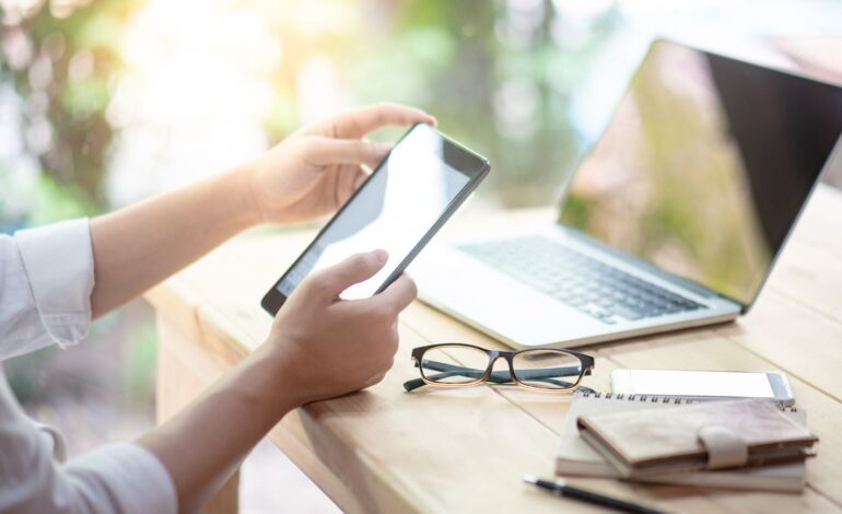 Hände einer Person mit Smartphone, die eine Kündigung per WhatsApp verfasst. Vor ihr auf dem Schreibtisch ein Laptop, eine Brille, ein Geldbeutel.